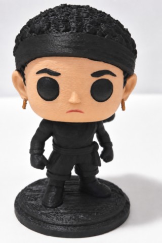 Figurine corse 3D Moru de 9 cm vue de face, avec cheveux noirs bouclés, bandeau noir, boucles d’oreilles dorées et tenue noire. moru-figurine-corse-3d-corsica-pop-vue-face-fabbrica-corsa